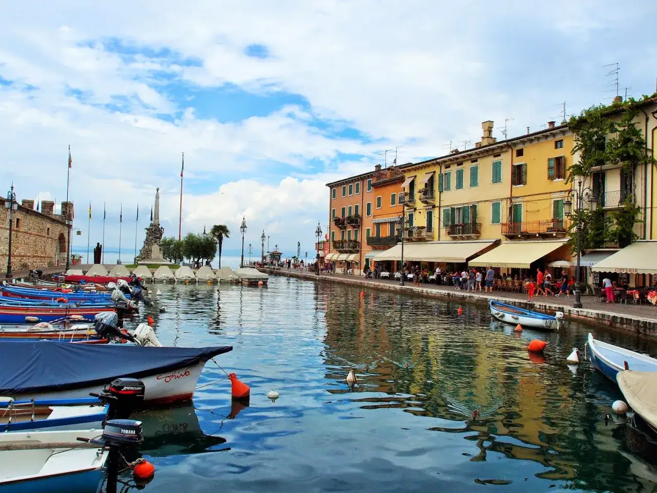 Un incantevole scorcio di Lazise o Bardolino, con barche ormeggiate e case colorate che si specchiano sull'acqua tranquilla.