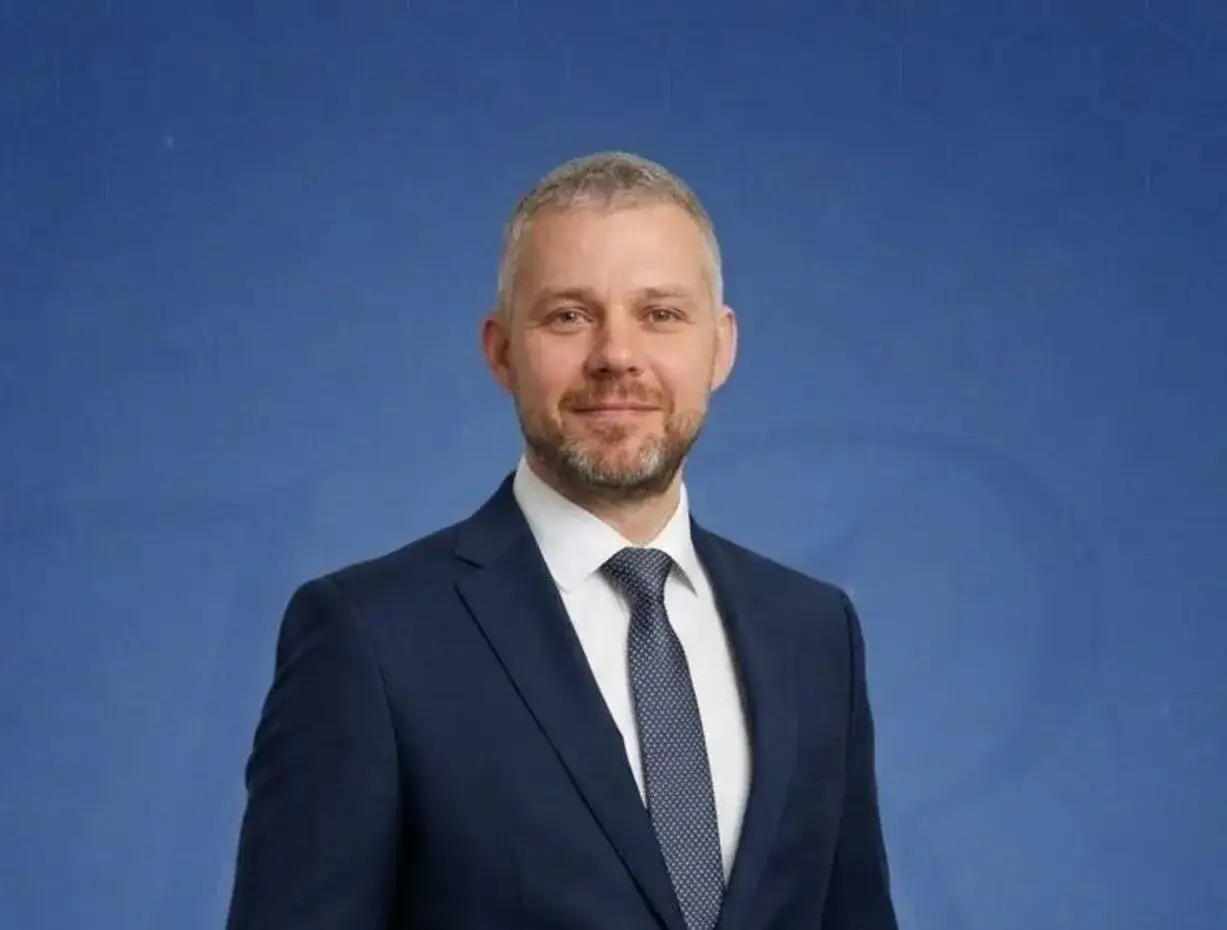 Portret mężczyzny w granatowym garniturze i krawacie na niebieskim tle z geometrycznym wzorem.