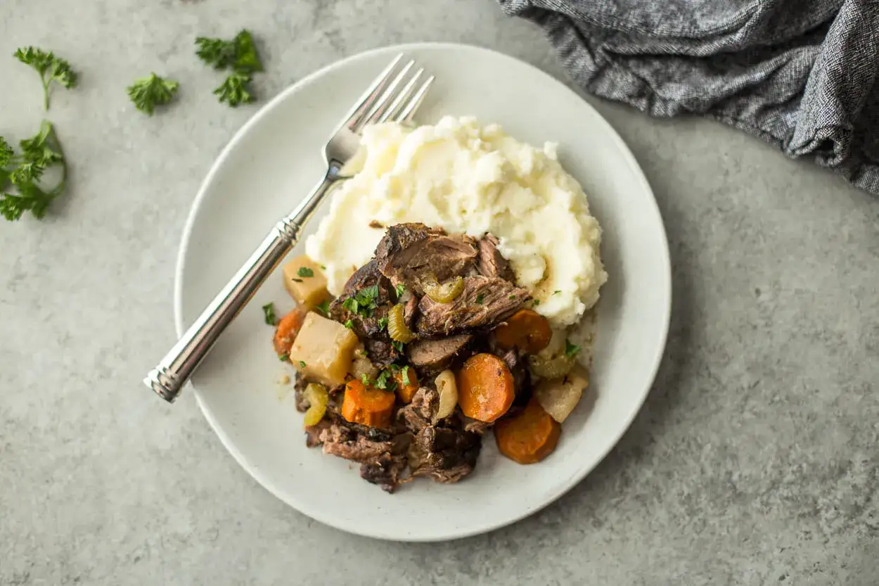 Un plato de carne deshebrada con zanahorias y patatas, acompañado de un cremoso puré de patatas.