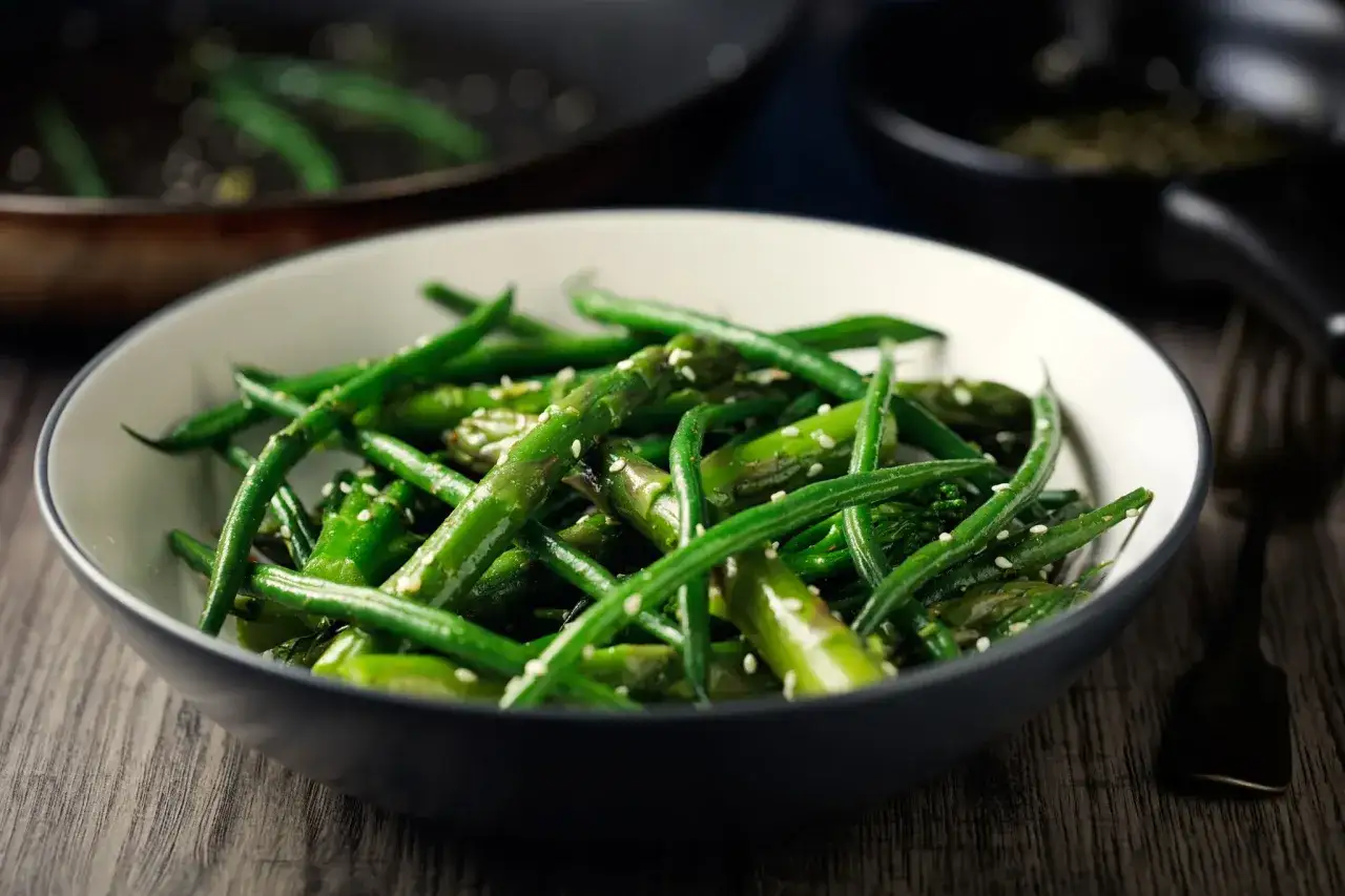 Un bol de haricots verts et d'asperges, parsemé de graines de sésame. Une recette haricot vert simple et savoureuse.