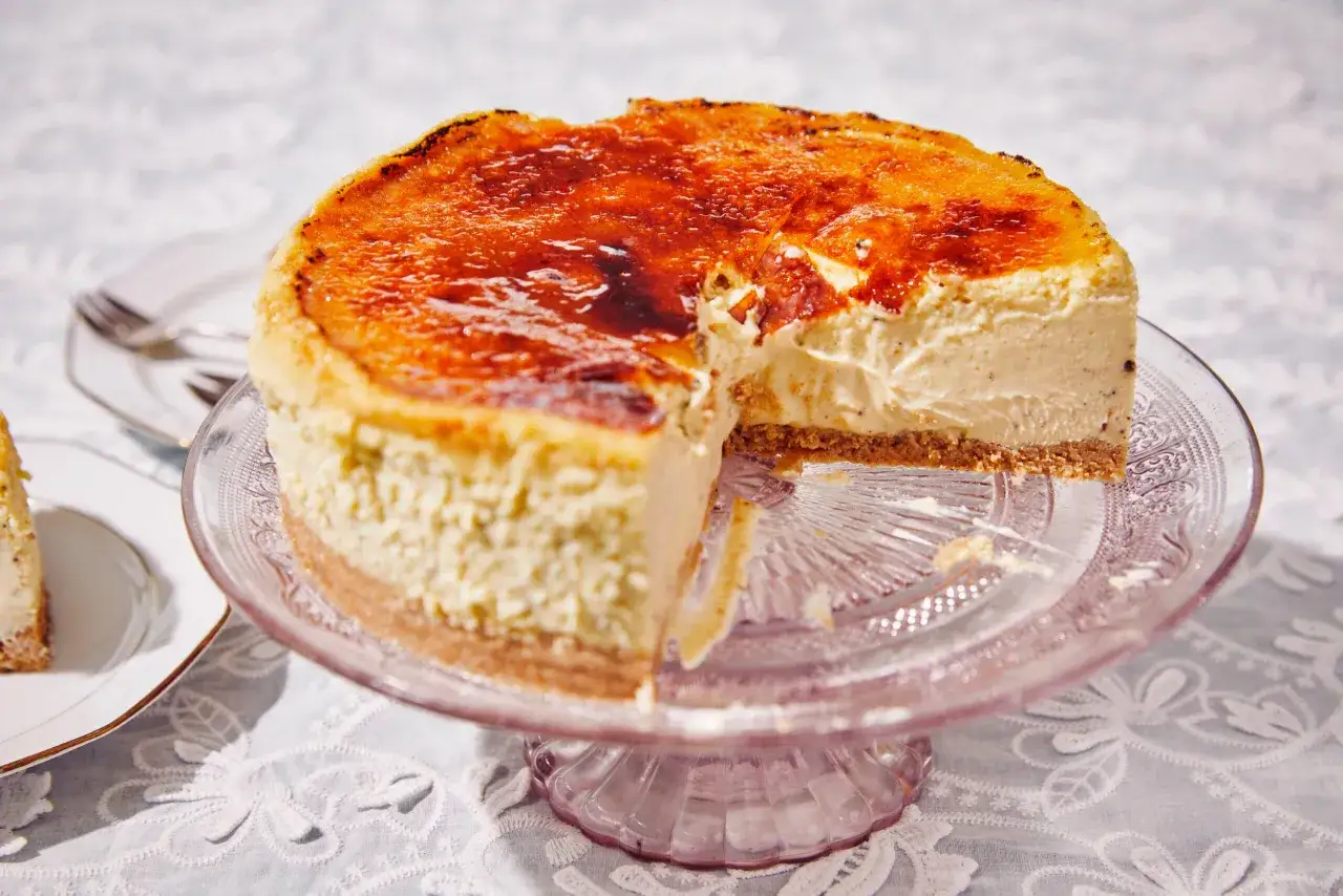 Un d&eacute;licieux cheesecake basque, &agrave; la cro&ucirc;te caram&eacute;lis&eacute;e et &agrave; la garniture cr&eacute;meuse, est servi sur un plat en verre rose. Une part a &eacute;t&eacute; retir&eacute;e.