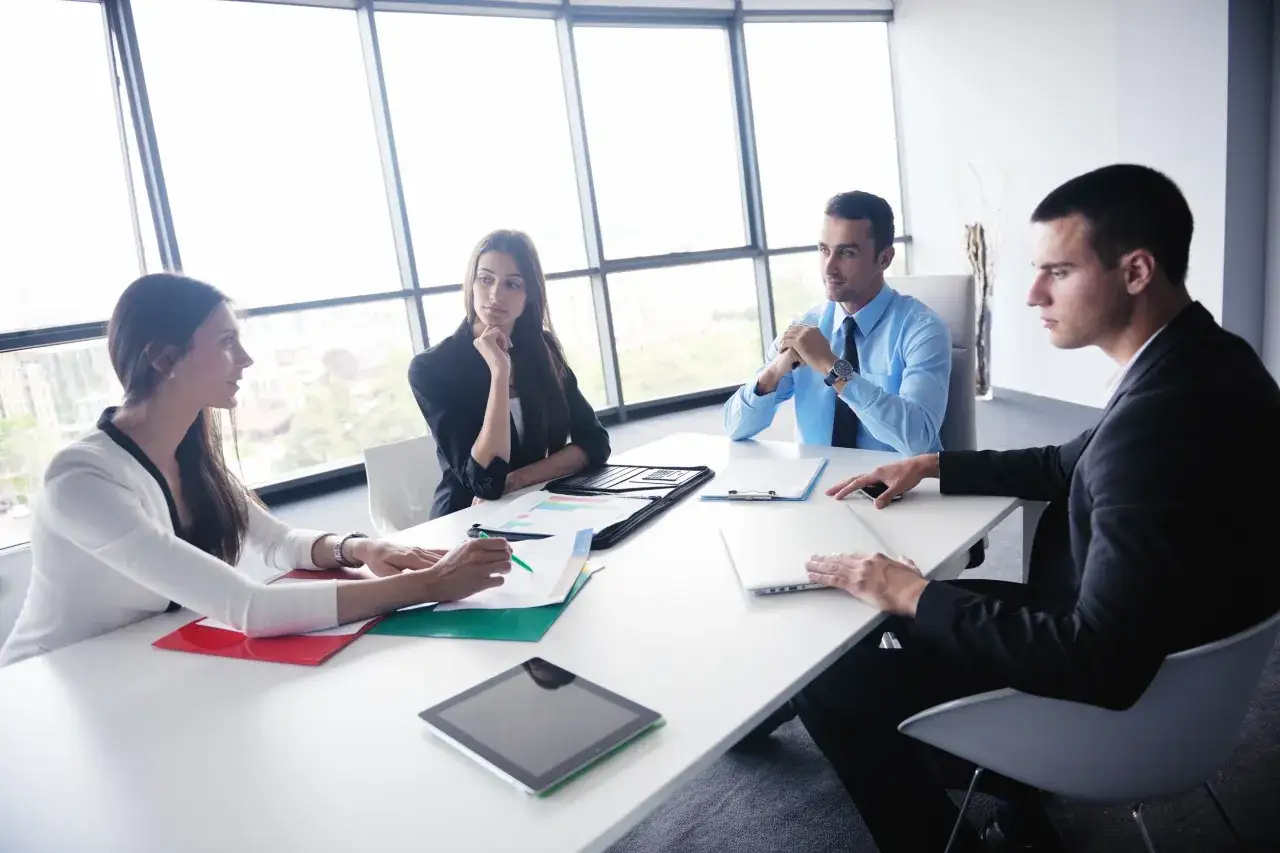 Riunione d'affari con quattro persone. Lo stress lavoro correlato &egrave; un rischio da valutare, ma la collaborazione pu&ograve; alleggerirlo.