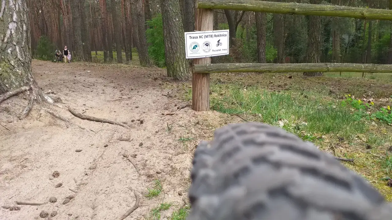 Leśna ścieżka, idealna na rowerowy **gravel po ł&oacute;dzku**. W tle widać ludzi i tabliczkę 