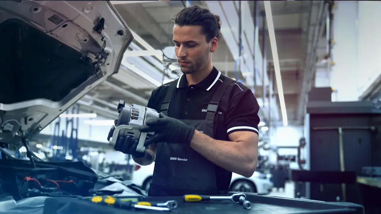 Mechanik samochodowy w serwisie BMW analizuje część, zastanawiając się, ile zarabia elektronik samochodowy.