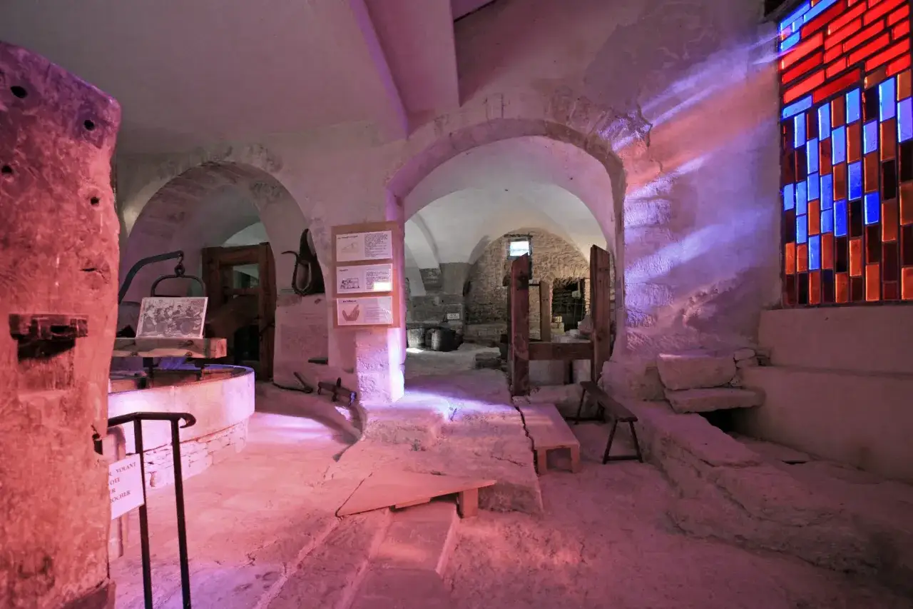 Intérieur du musée du vitrail à Gordes, avec des arches en pierre, un vitrail coloré et des expositions sur l'histoire du verre.