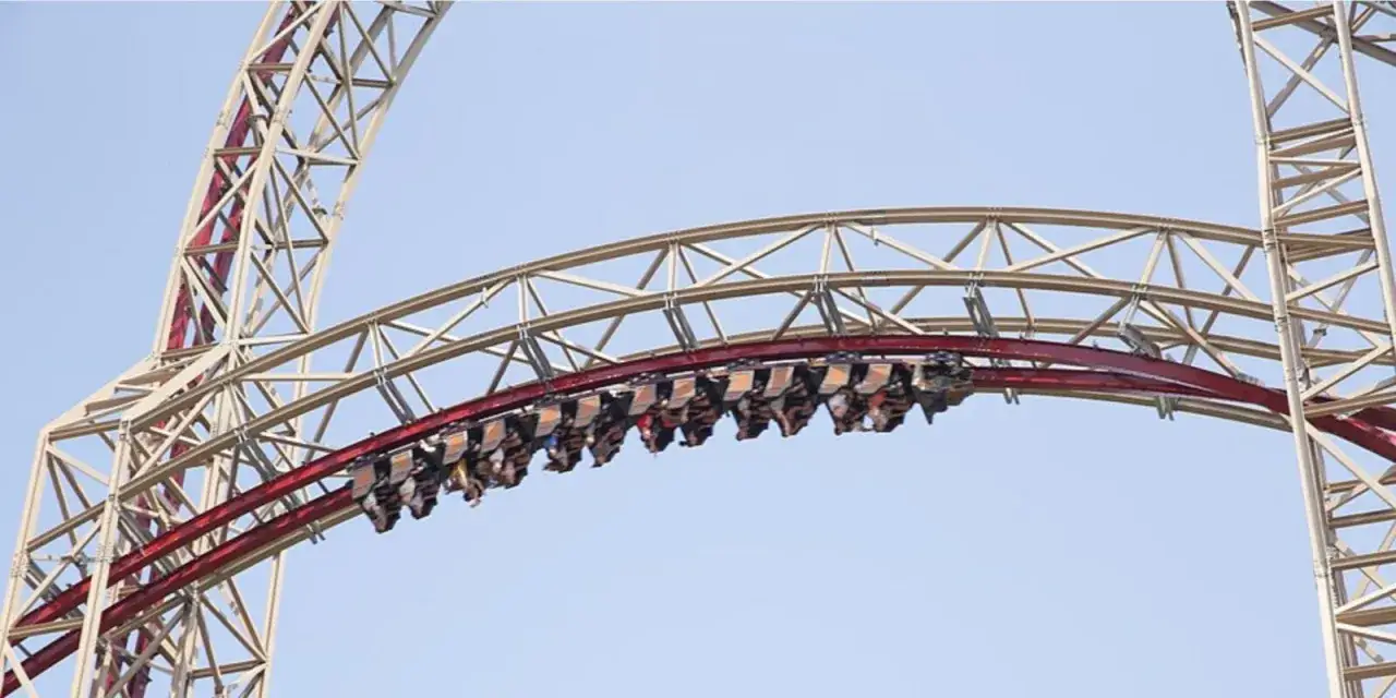 Pasażerowie jadą na szczycie największego rollercoastera w Polsce, gotowi na ekscytującą podróż.