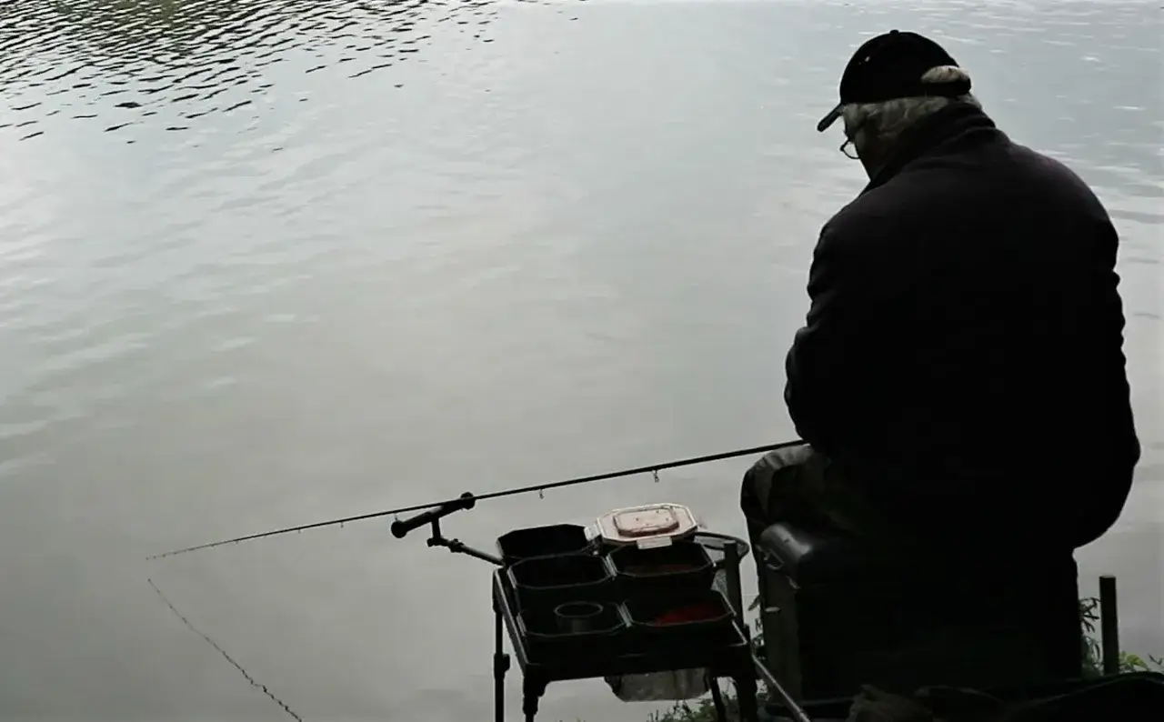 Ein Angler sitzt am Wasser und wartet mit seiner Feederrute auf einen Biss. Die Feederrute ist ideal f&uuml;r diese Art des Angelns.