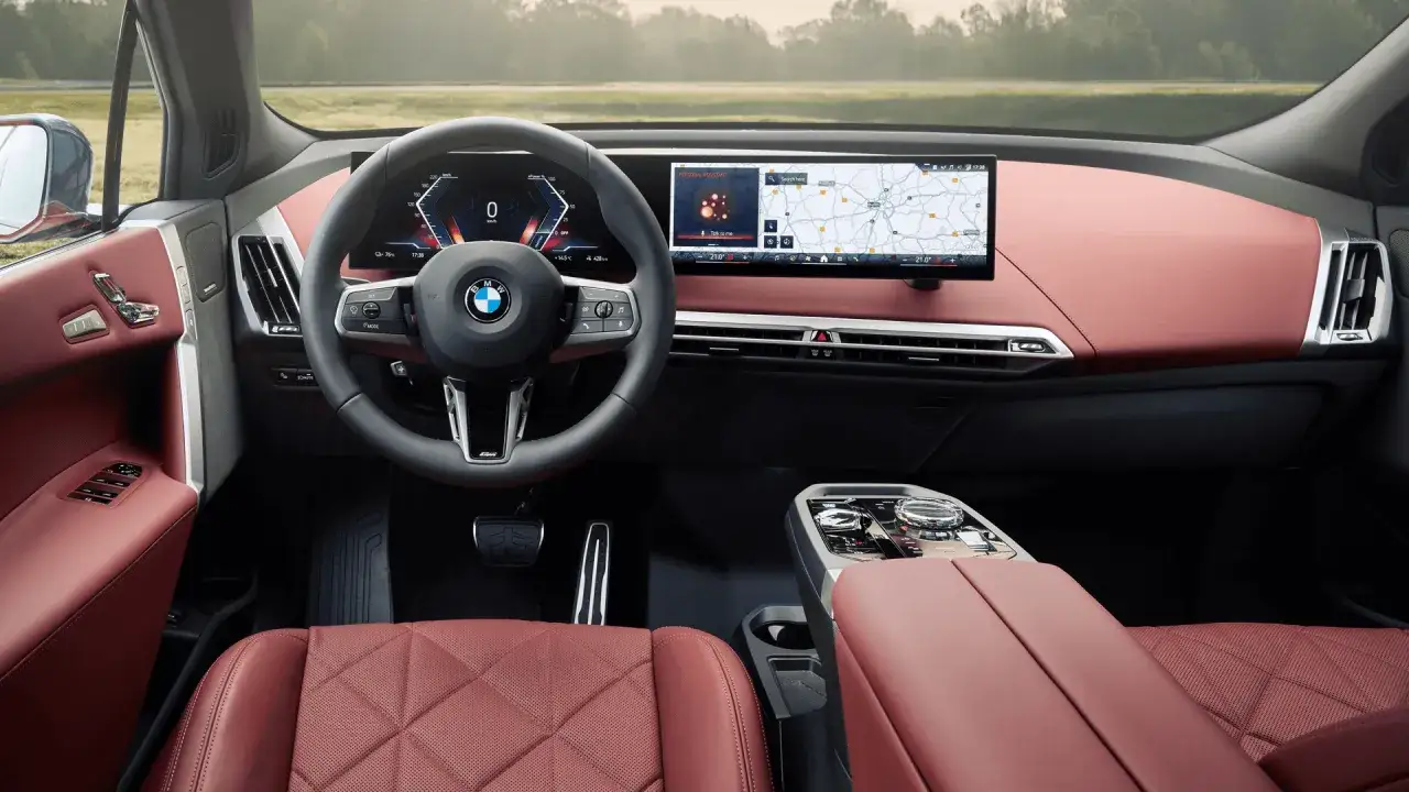 Wnętrze BMW iX z czerwonymi skórzanymi fotelami i nowoczesnym panelem sterowania. Kierownica z wyświetlaczem cyfrowym i ekranem nawigacji.