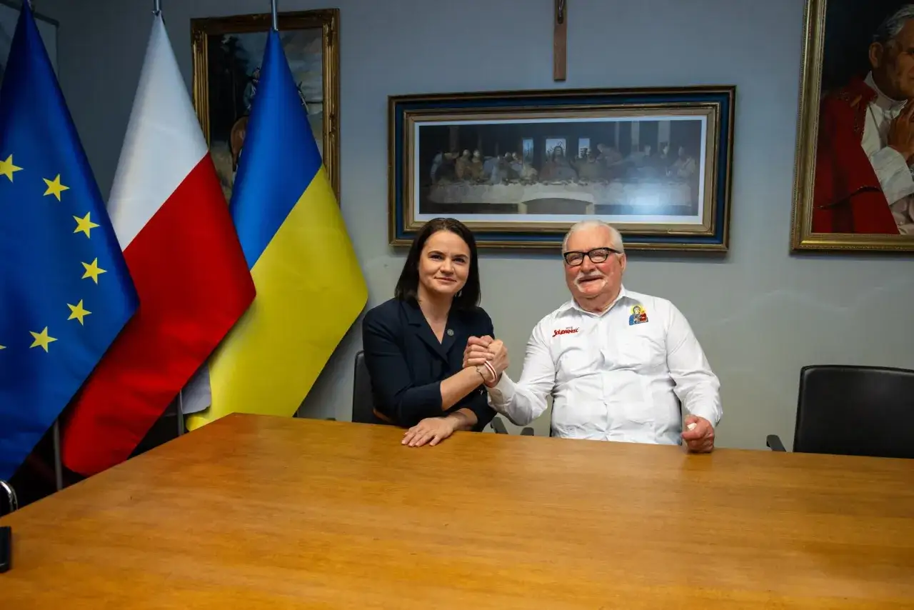 Lech Wałęsa, symbole de la lutte pour la libert&eacute;, serre la main d'une jeune femme devant les drapeaux polonais, ukrainien et europ&eacute;en.