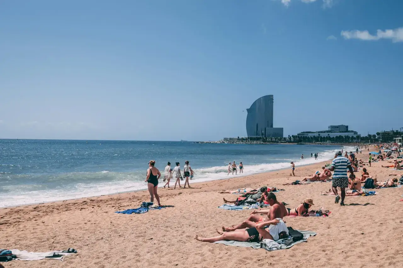 Gente disfrutando de un d&iacute;a soleado en una de las mejores playas de Barcelona, con el Hotel W de fondo.