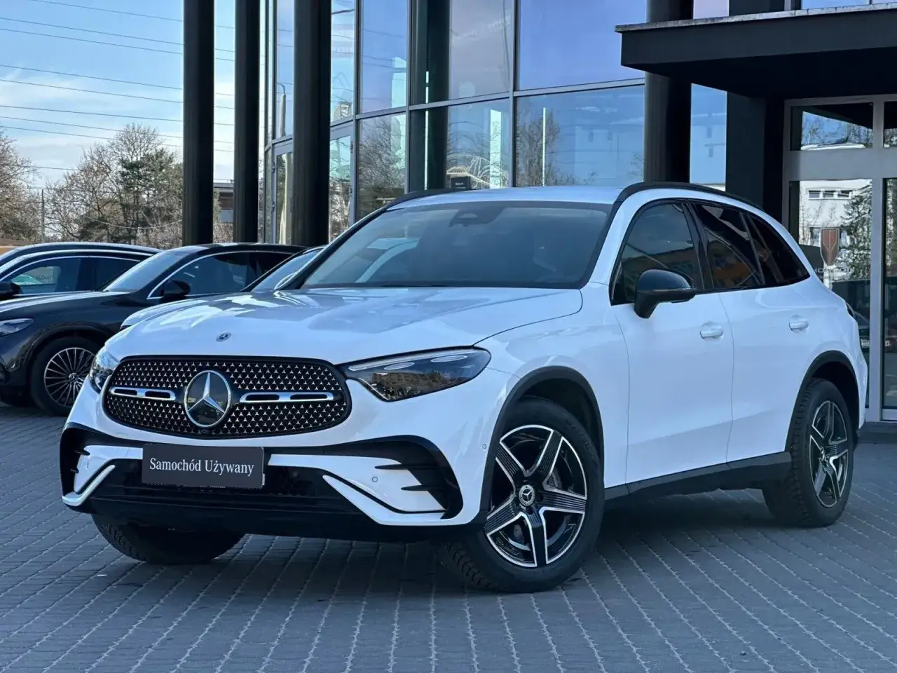 Biały, używany Mercedes GLC z salonu, prezentujący się elegancko na tle nowoczesnego budynku.