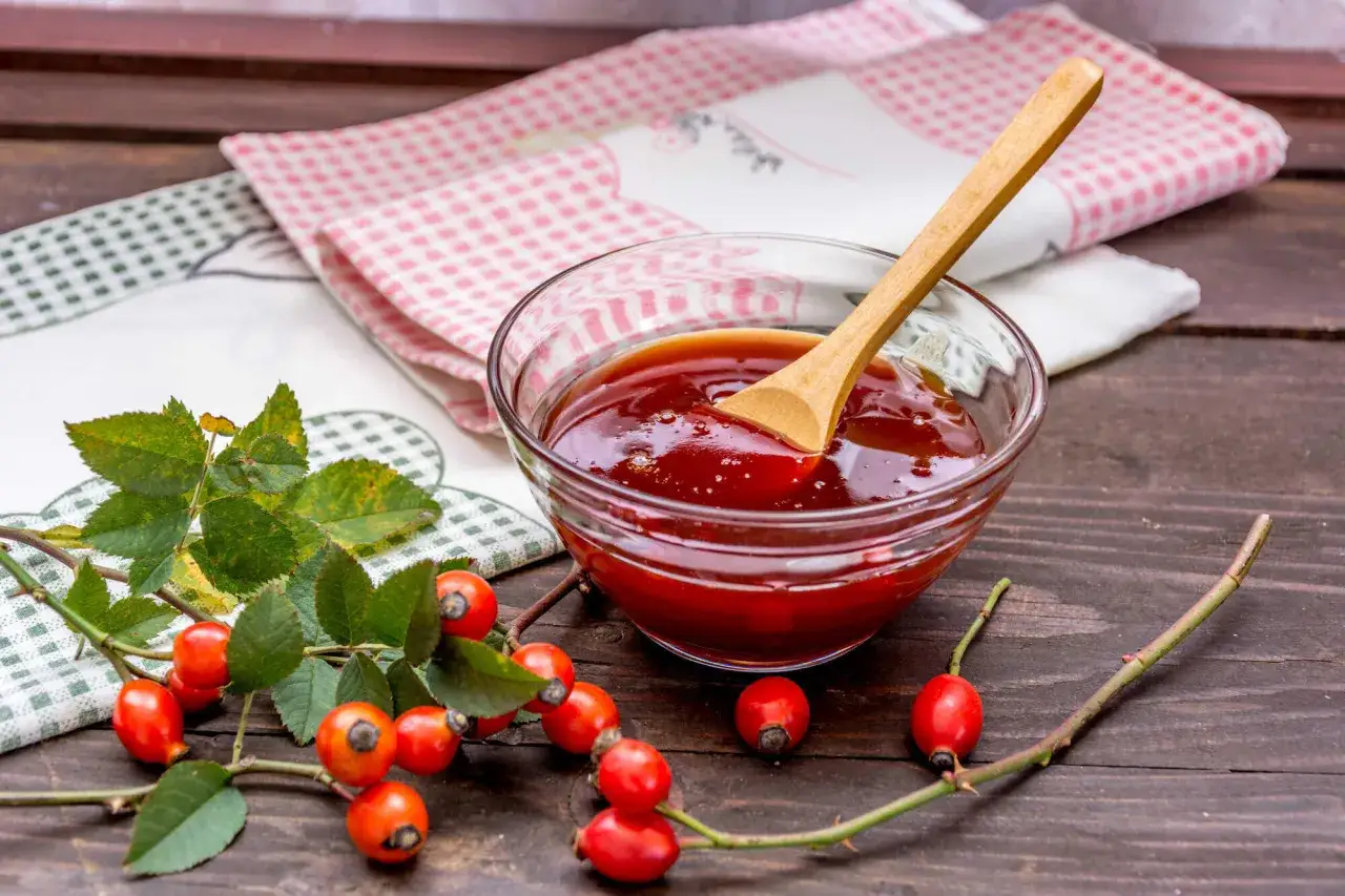 Frischer Hagebutten-Aufstrich in einer Glasschale, bereit f&uuml;r k&ouml;stliche Hagebutten Rezepte. Daneben liegen frische Hagebutten.