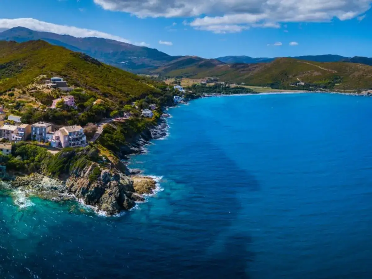 Ein malerischer **Strand in Frankreich** mit t&uuml;rkisfarbenem Wasser, gr&uuml;nen H&uuml;geln und charmanten H&auml;usern, die sich an die K&uuml;ste schmiegen.