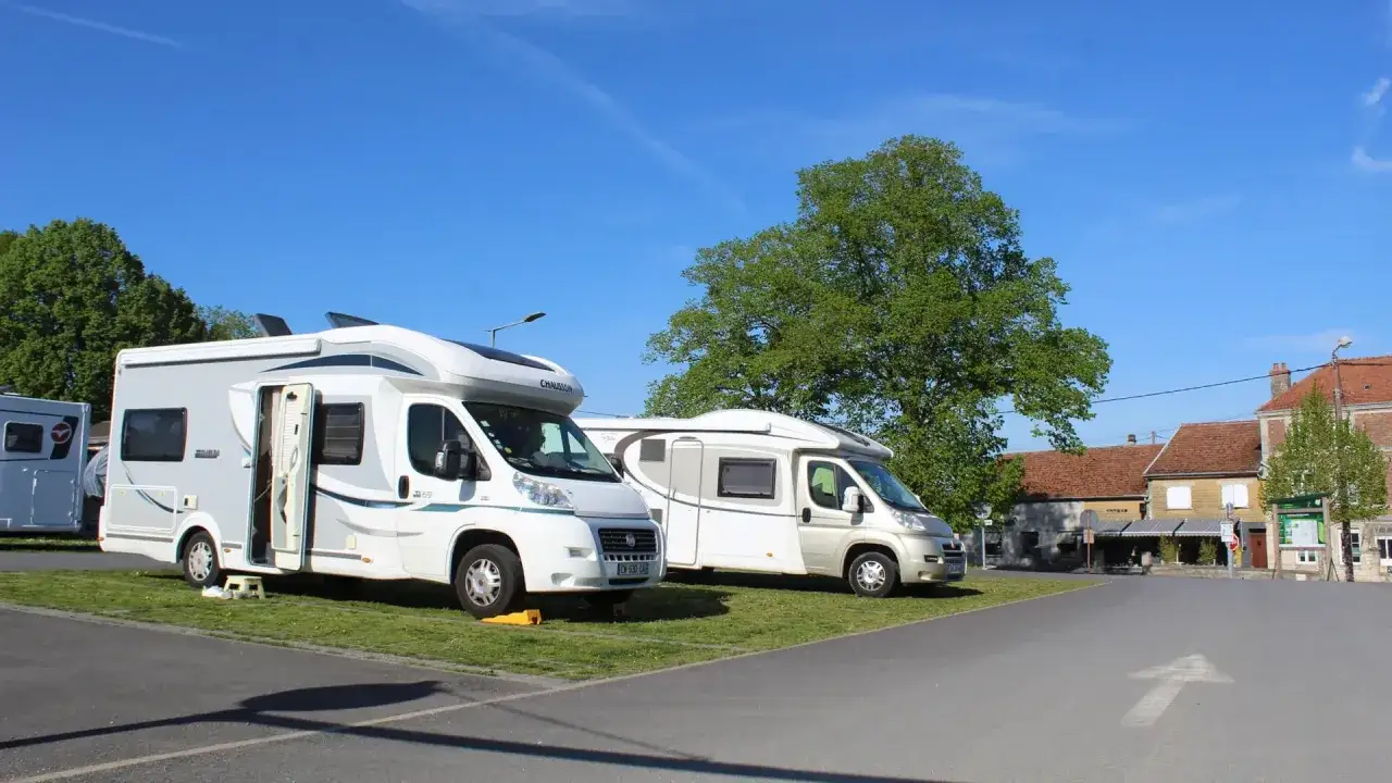 Un spot de camping-car sauvage avec plusieurs véhicules stationnés sur une pelouse, sous un ciel bleu clair.