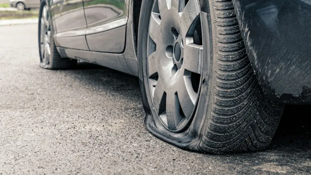 Une voiture est immobilisée, un pneu complètement à plat. Impossible de rouler avec un pneu crevé, il faut le changer.