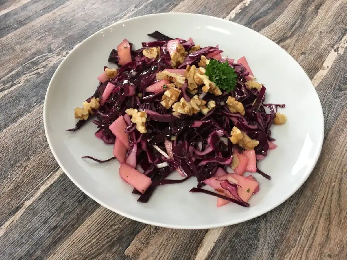 Ein bunter rotkohl salat mit Apfelstücken und Walnüssen, garniert mit Petersilie, auf einem weißen Teller.