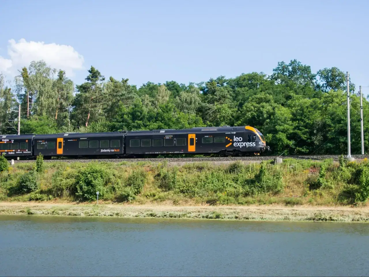 Czarny pociąg Leo Express z pomarańczowymi detalami jedzie wzdłuż zielonego brzegu. Szukasz tanich biletów PKP Warszawa - Kraków?