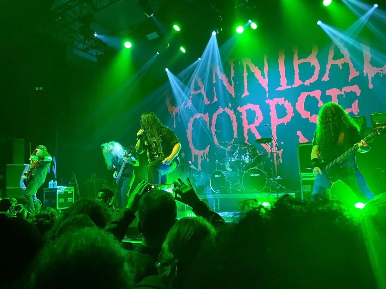 Le groupe Cannibal Corpse en concert, éclairé par des lumières vertes et blanches. La foule est en délire.