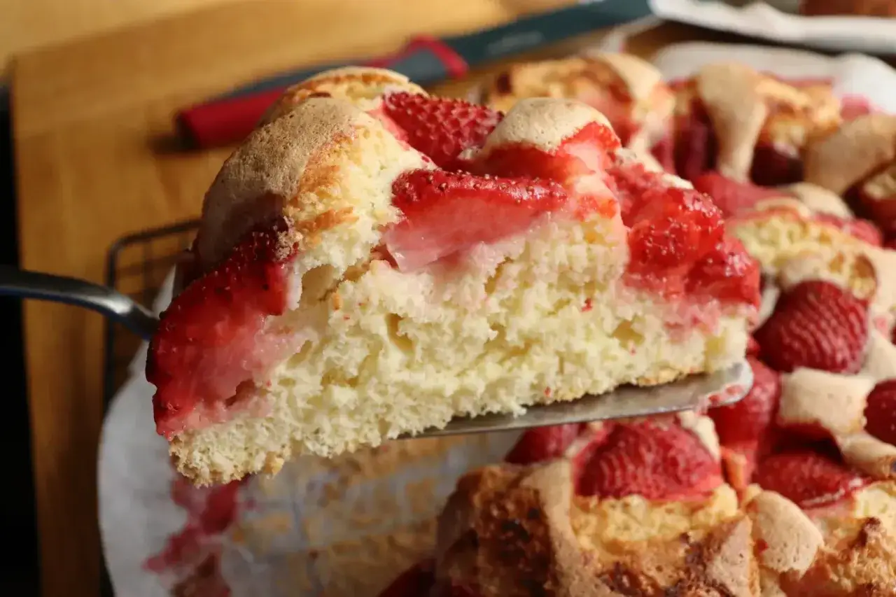 Ein Stück saftiger Erdbeerkuchen wird aus einer ganzen Tarte gehoben. Dieses Erdbeerboden Rezept ist ein Genuss!