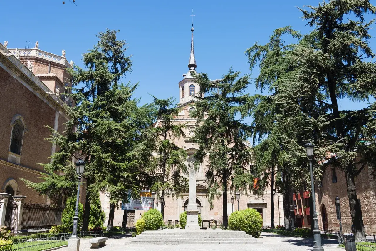 Fachada de un edificio hist&oacute;rico con un campanario, rodeado de &aacute;rboles frondosos. Un lugar que evoca la paz de los monasterios cerca de Madrid.