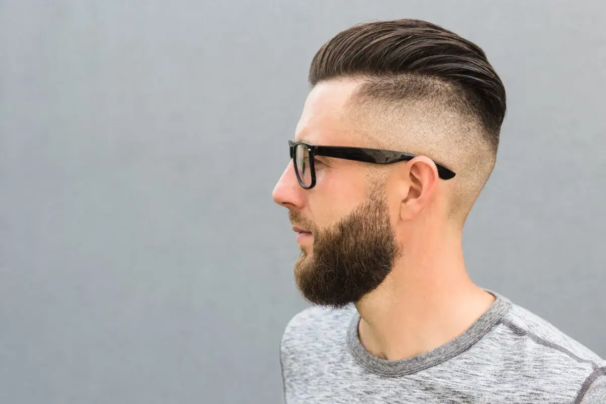 Mężczyzna z zarostem i modnym buzz cut, który subtelnie podkreśla zakola.
