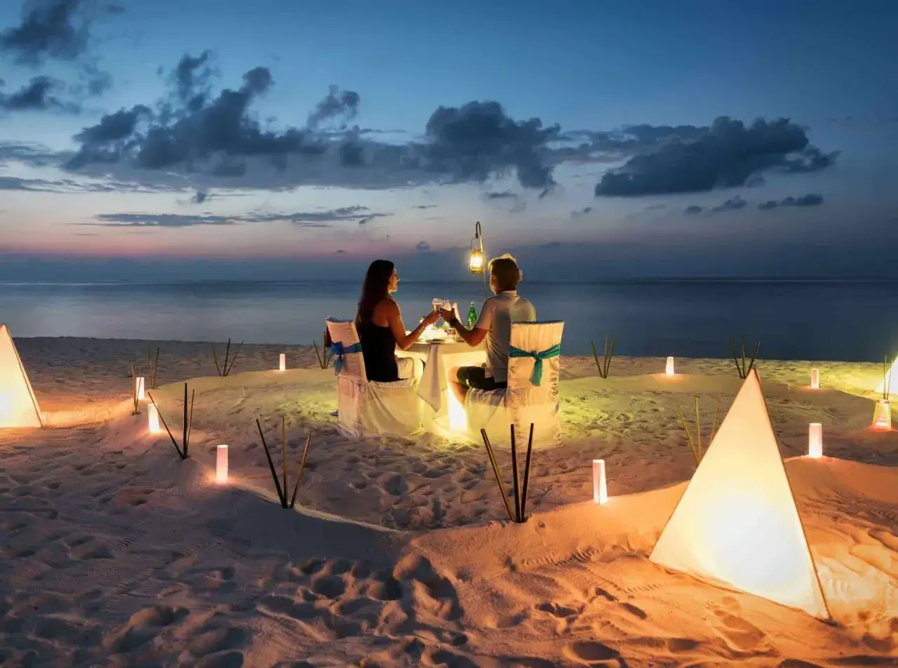 Romantyczna kolacja na plaży podczas podróży poślubnej. Para wznosi toasty przy świecach i lampionach.