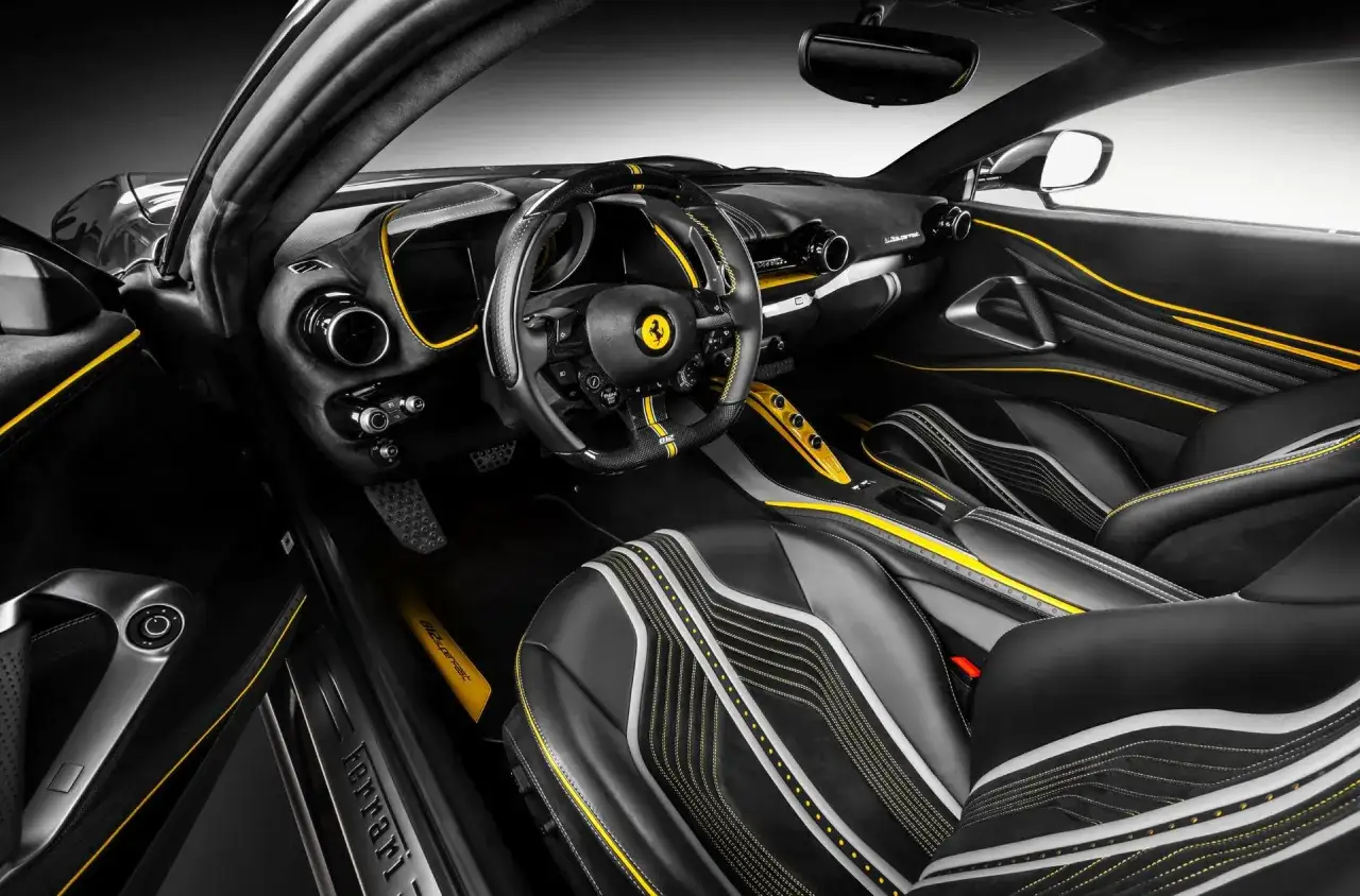 Wnętrze Ferrari w czerni i ż&oacute;łci, z wyścigowymi fotelami i kierownicą. Tak wygląda ferrari z bliska.