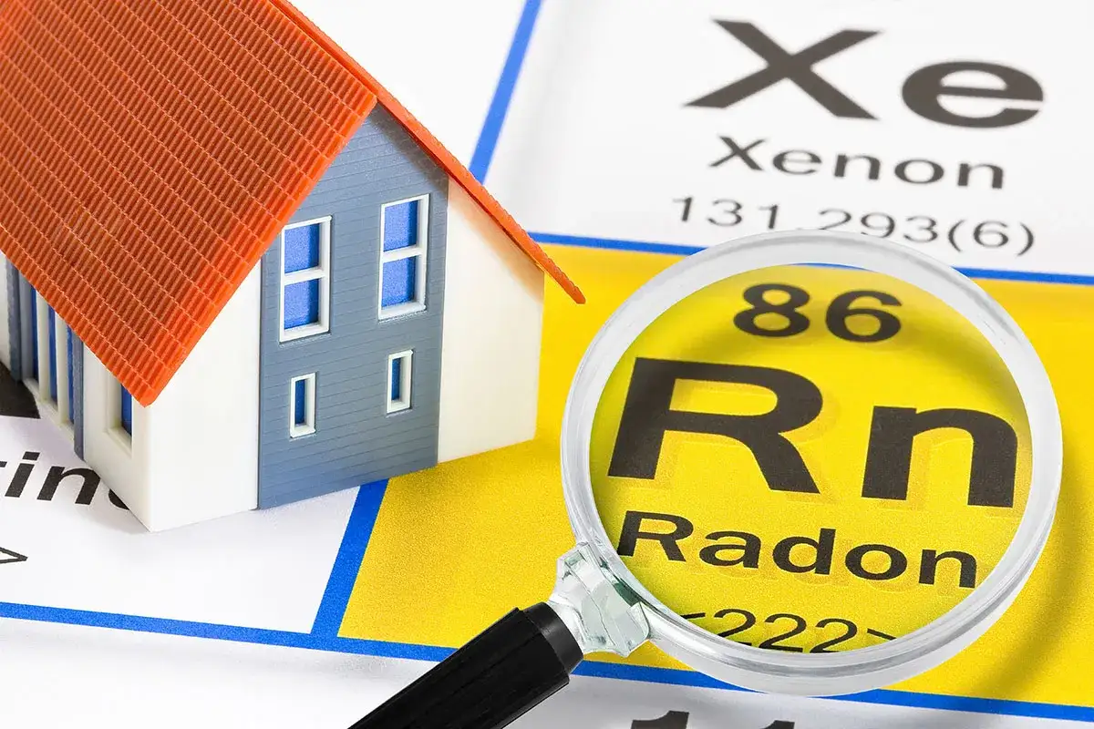 En modell av ett hus unders&ouml;ks med ett f&ouml;rstoringsglas som visar grund&auml;mnet radon.