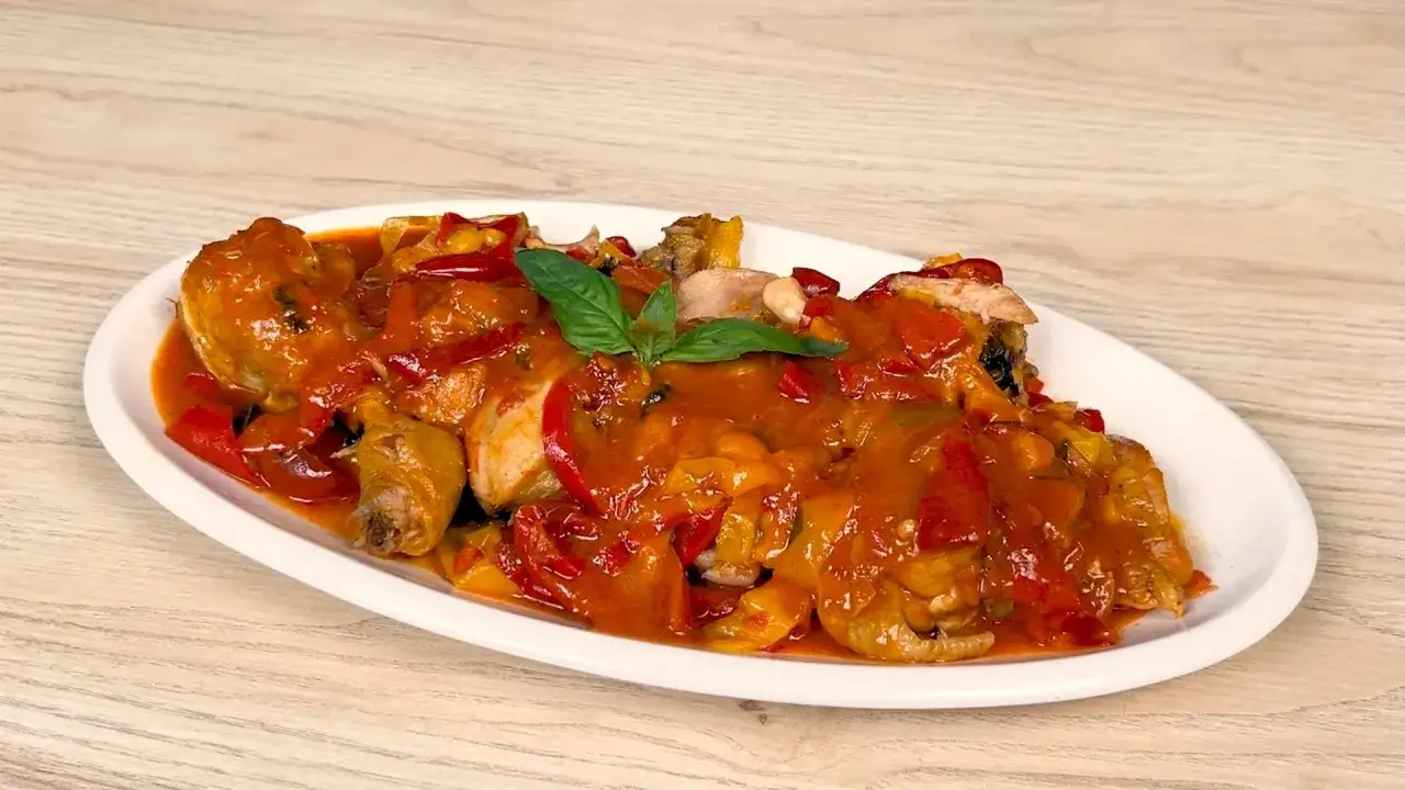 Pollo e peperoni alla romana, un piatto succulento con pezzi di pollo e peperoni rossi e gialli in salsa, guarnito con basilico.