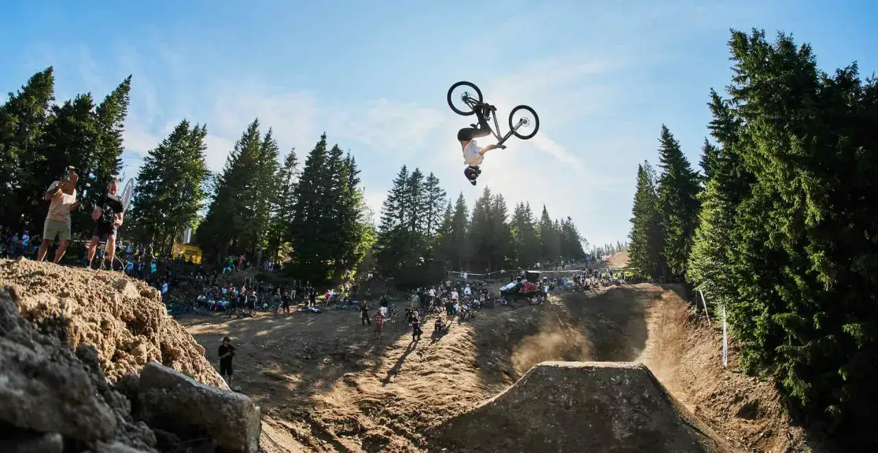 Ein Mountainbiker vollf&uuml;hrt einen R&uuml;ckw&auml;rtssalto in der Luft, w&auml;hrend Zuschauer am Rand eines **Bikepark Tschechien** jubeln.