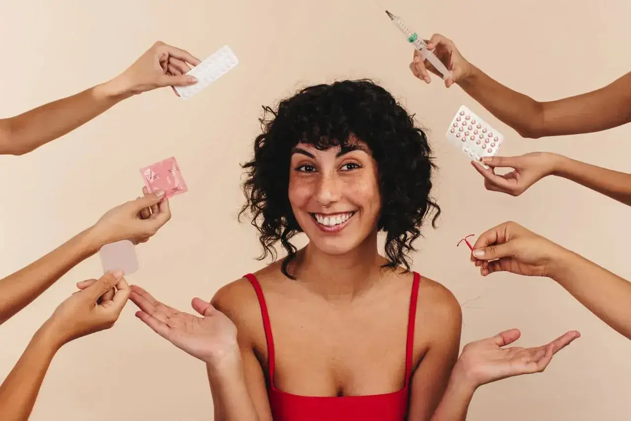 Une femme souriante entour&eacute;e de mains proposant pilules, st&eacute;rilet, patch, pr&eacute;servatif et seringue. Un choix de contraception, peut-&ecirc;tre pour la fin de la m&eacute;nopause.
