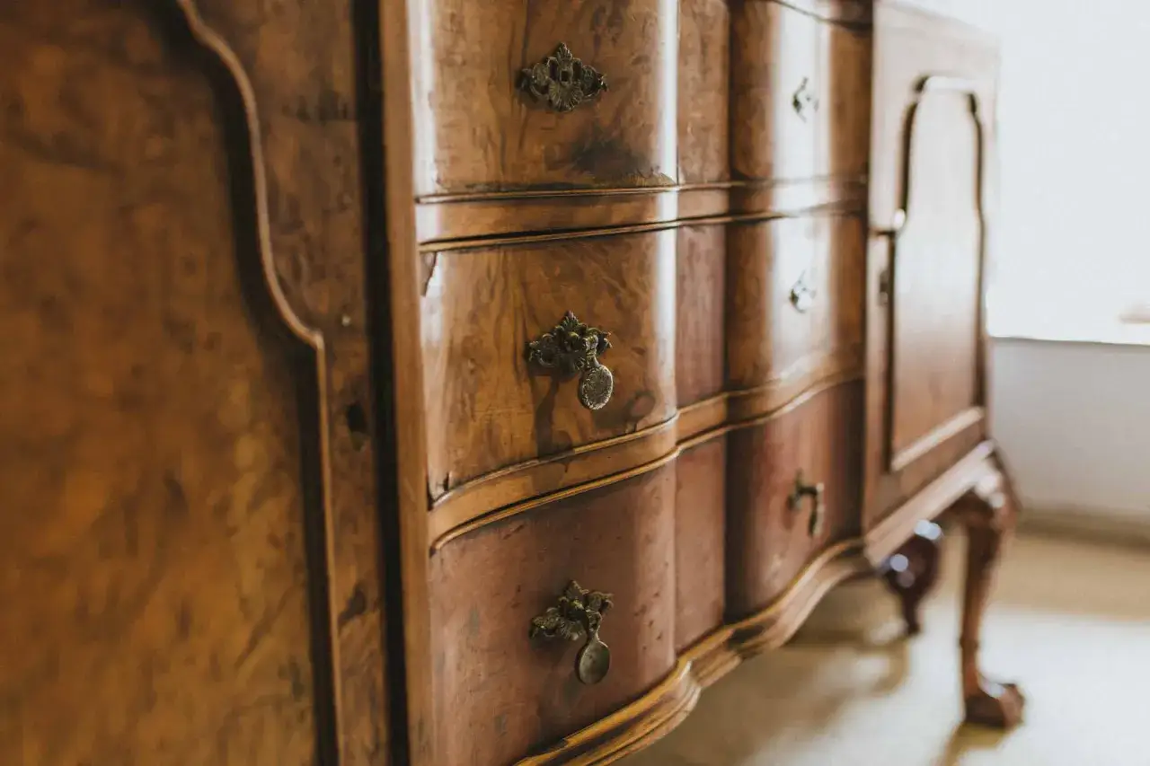 Cassettiera antica con maniglie ornate, che mostra una ricca tabella colori legno naturali.