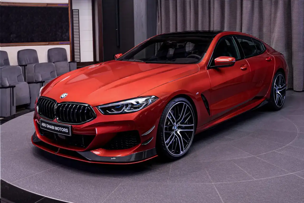 Ognisty czerwony BMW 840i z czarnym dachem i felgami, prezentowany w salonie Abu Dhabi Motors.