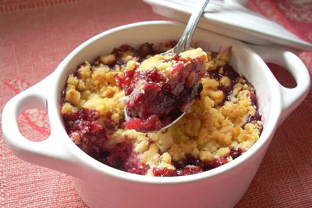 Une cuill&egrave;re pr&eacute;l&egrave;ve une portion g&eacute;n&eacute;reuse de crumble fruits rouges, r&eacute;v&eacute;lant la garniture juteuse et la p&acirc;te dor&eacute;e.