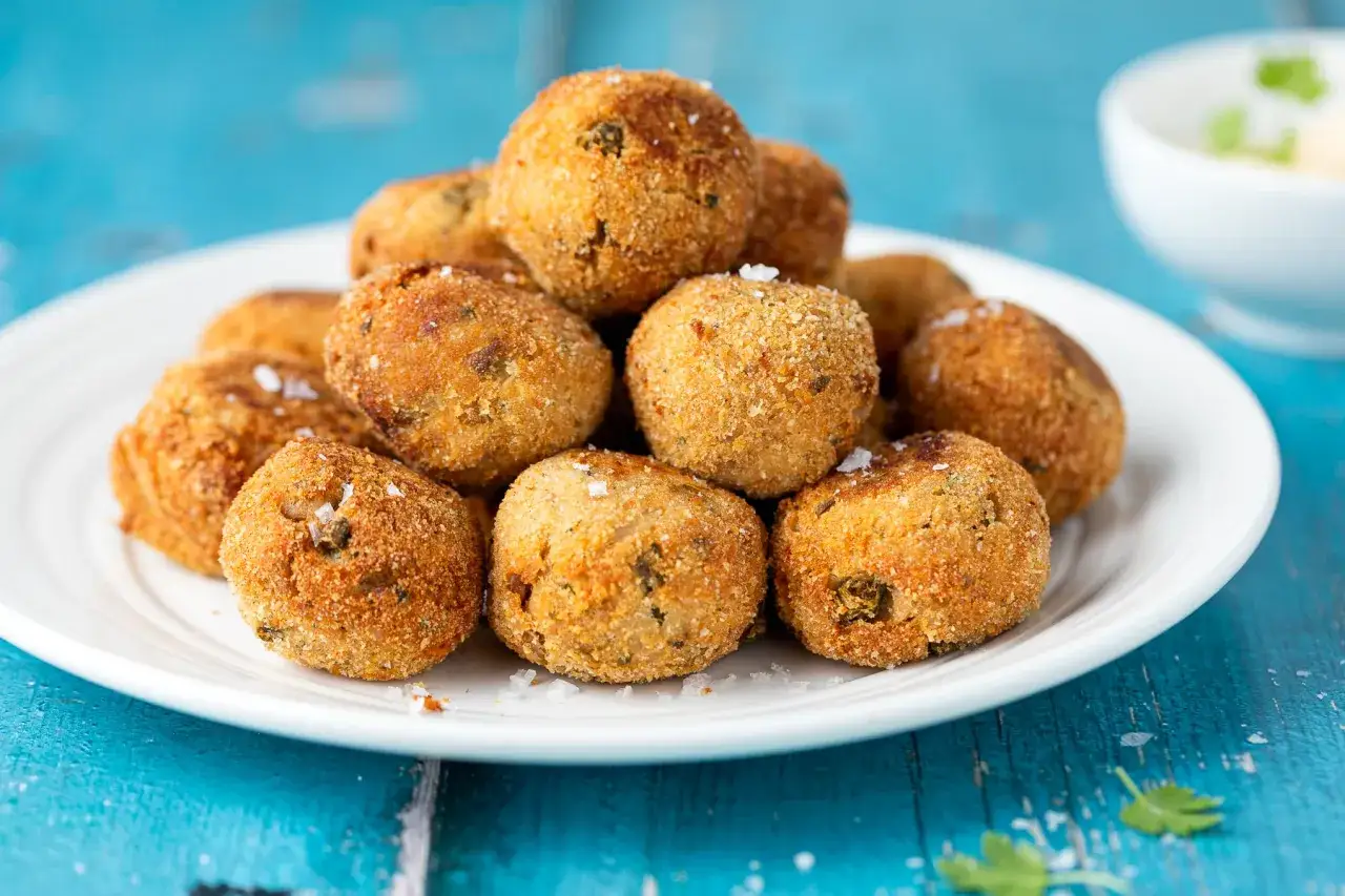 Pile di polpette tonno e ricotta dorate e croccanti, cosparse di sale grosso, su un piatto bianco.