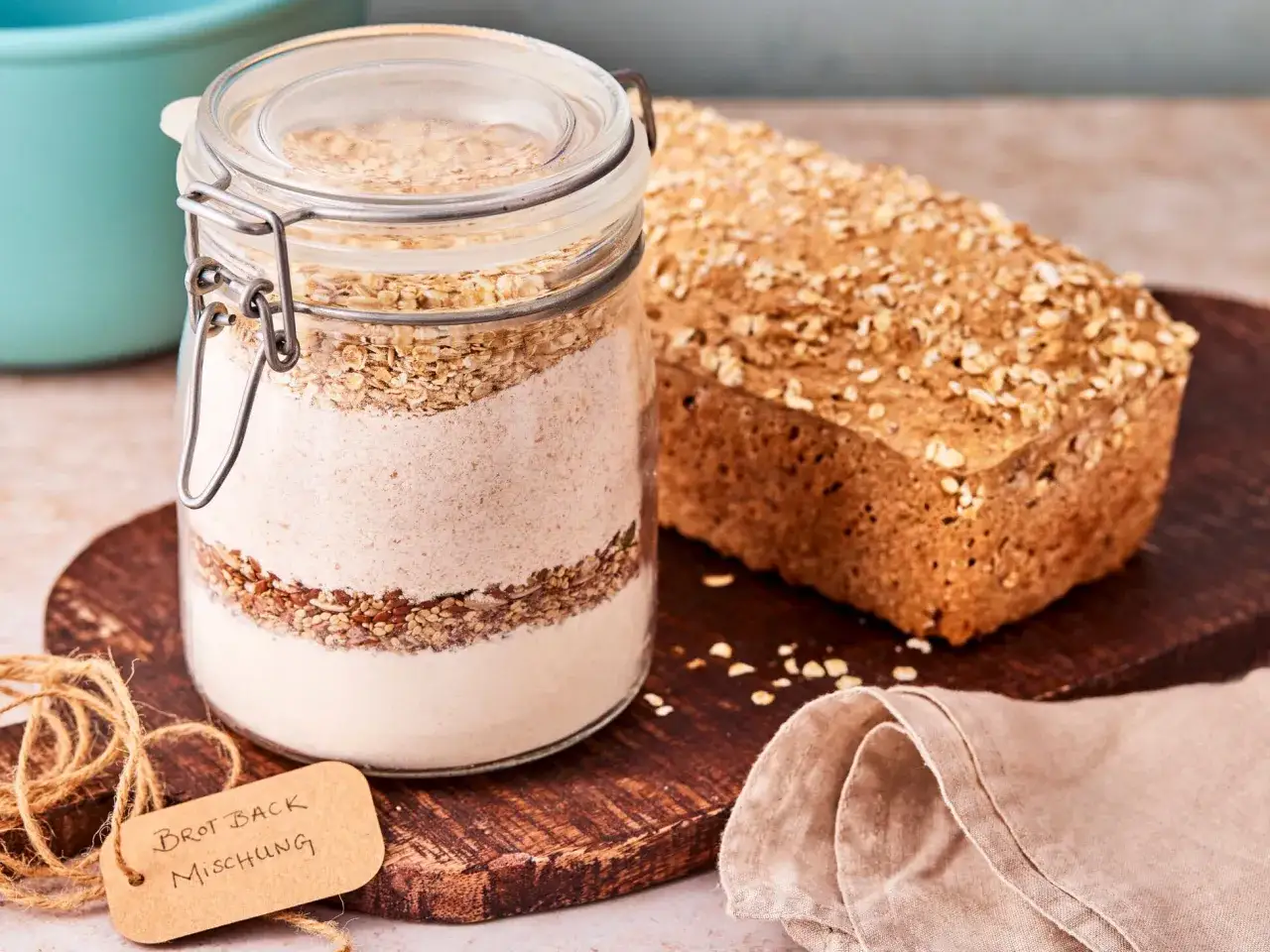 Glas mit Zutaten für Brotbackmischung selber machen, daneben ein fertiges Brot.
