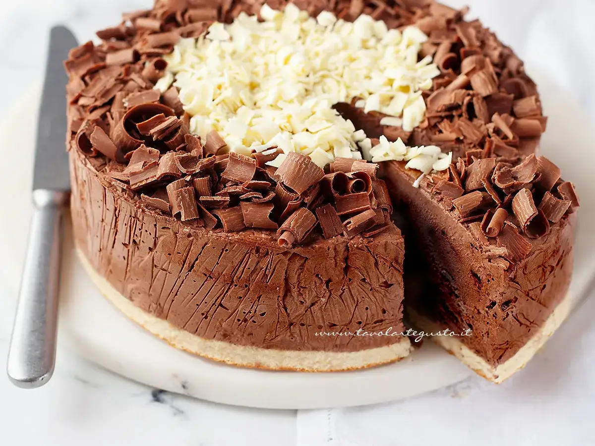 Delizioso semifreddo al cioccolato, ricoperto di riccioli di cioccolato fondente e bianco. Una fetta &egrave; stata tagliata, rivelando la sua consistenza cremosa.