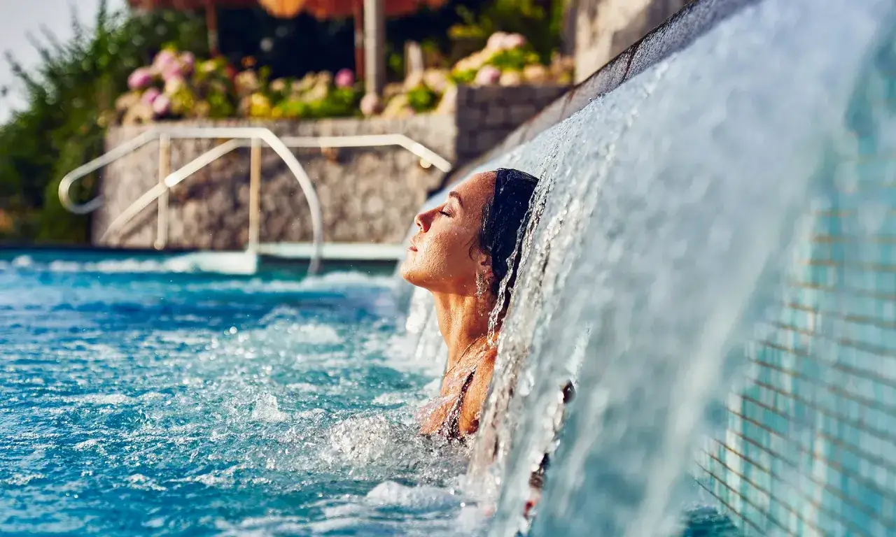 Donna rilassata sotto una cascata d'acqua in una piscina termale. Informarsi sulle acque termali Ischia controindicazioni prima di immergersi.