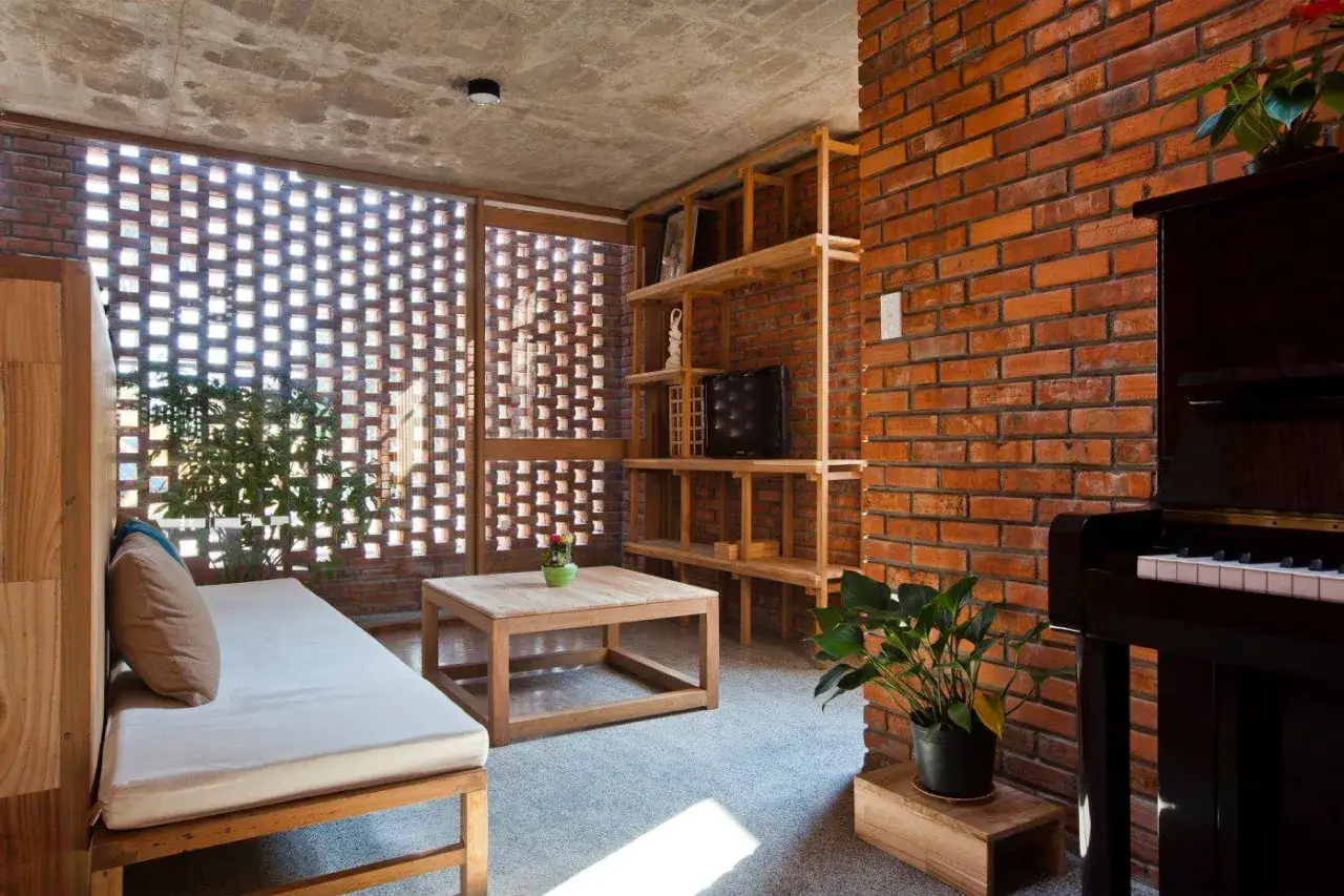Gemütliches Wohnzimmer mit Holzbänken, einem Holztisch und einem Klavier. Die Wand aus roten Ziegeln und die Fenster mit moc klemmbausteine-Muster schaffen eine warme Atmosphäre.