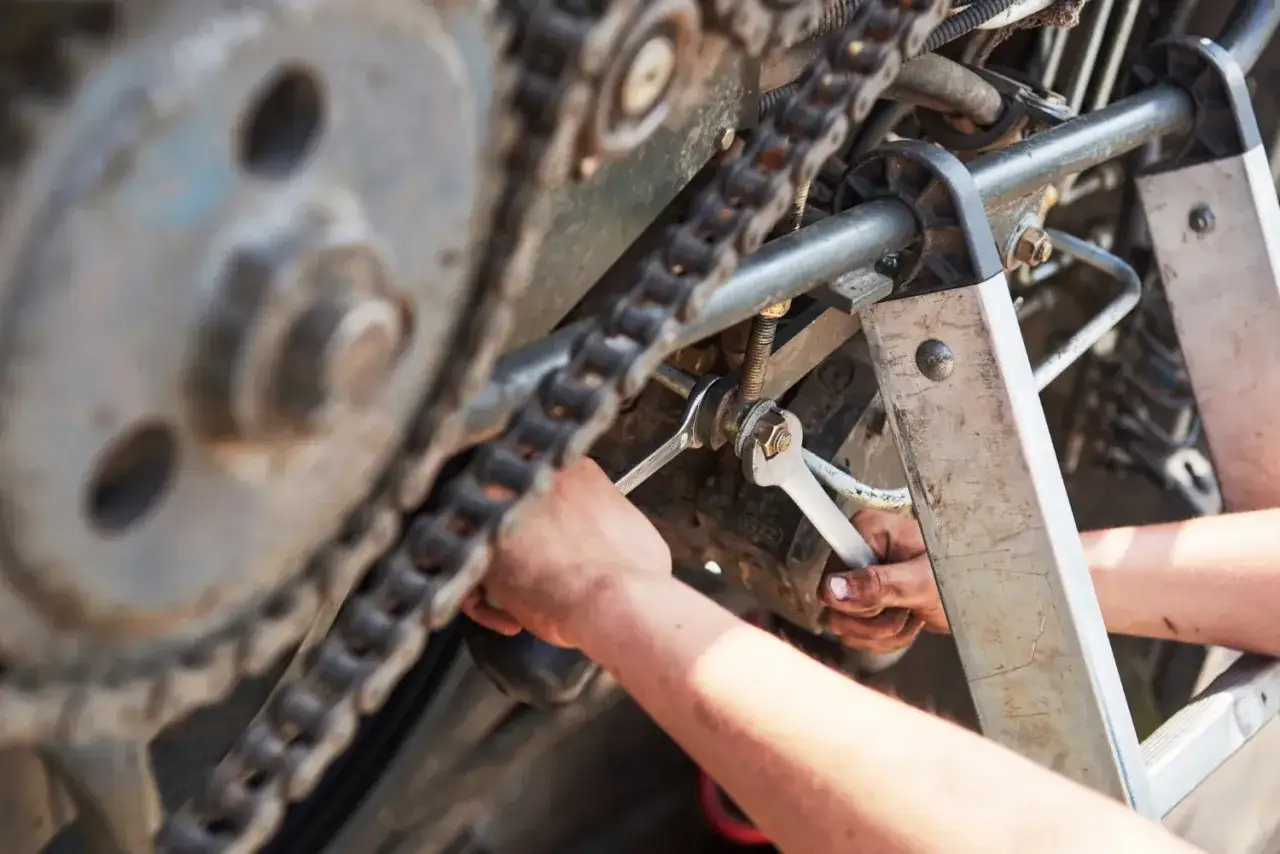 Mechanik dokręca śrubę przy łańcuchu napędowym, być może sprawdzając sprzęgło alternatora objawy.
