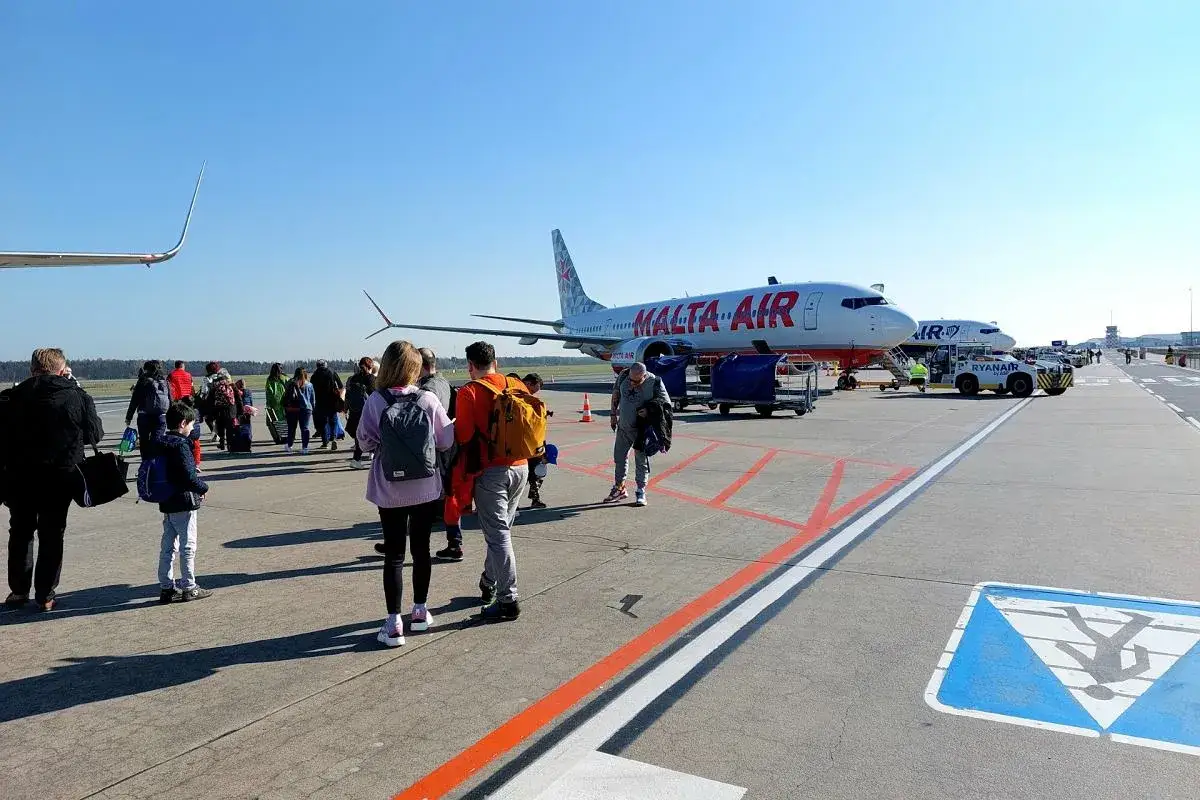 Pasażerowie czekają na samolot Malta Air na lotnisku. Sprawdzają rozkład lotów Modlin, gotowi do podróży.