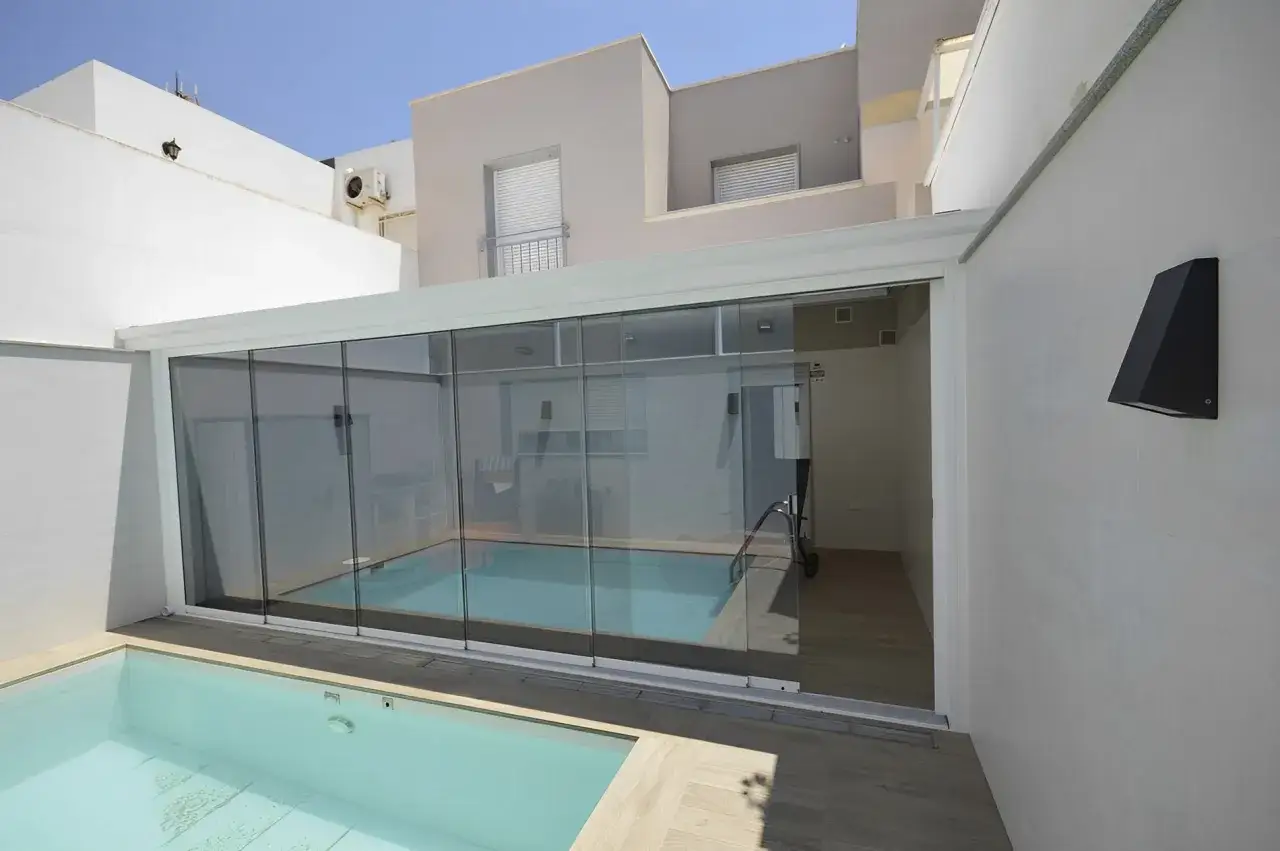 Modern patio with a pool enclosed by elegant cristales plegables, offering a seamless transition between indoor and outdoor living.