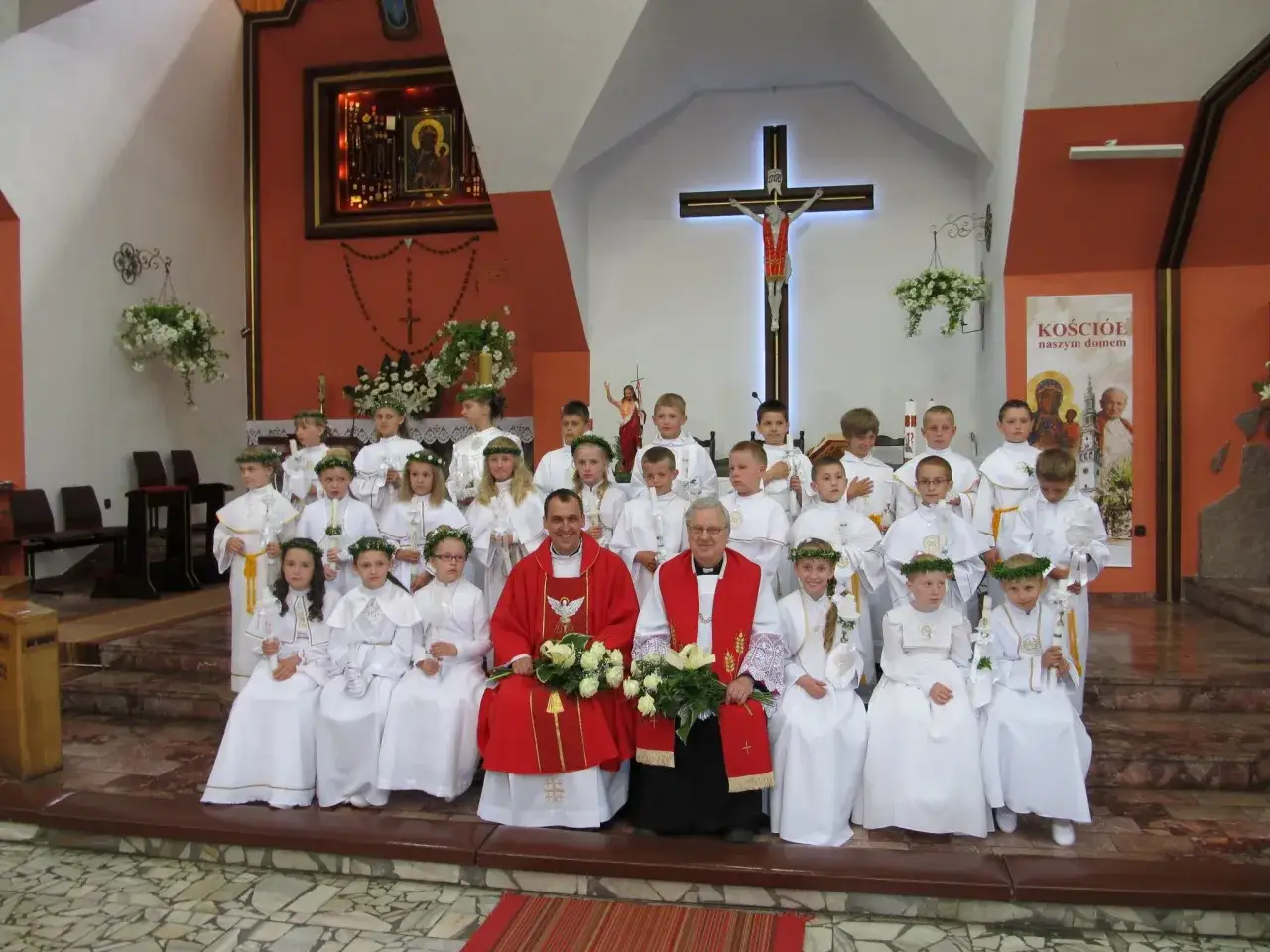 Proboszcz i ministranci w białych strojach podczas uroczystości w kościele.