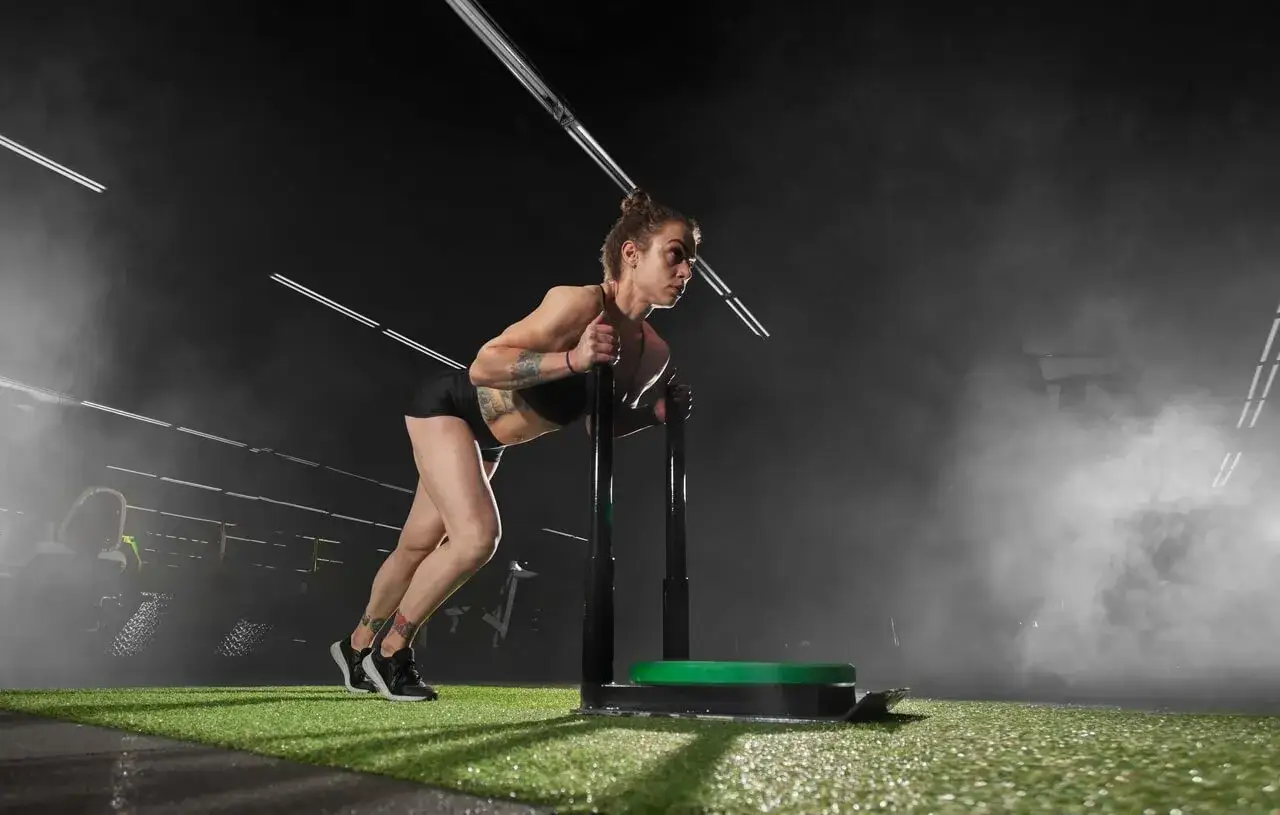 Kobieta pcha sanie treningowe. Intensywny trening, który może być częścią tego, ile trwa trening crossfit.