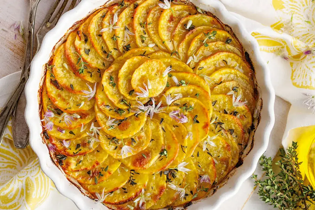 Tortino di patate dorato e profumato, guarnito con erbe aromatiche e fiori eduli, pronto per essere gustato.
