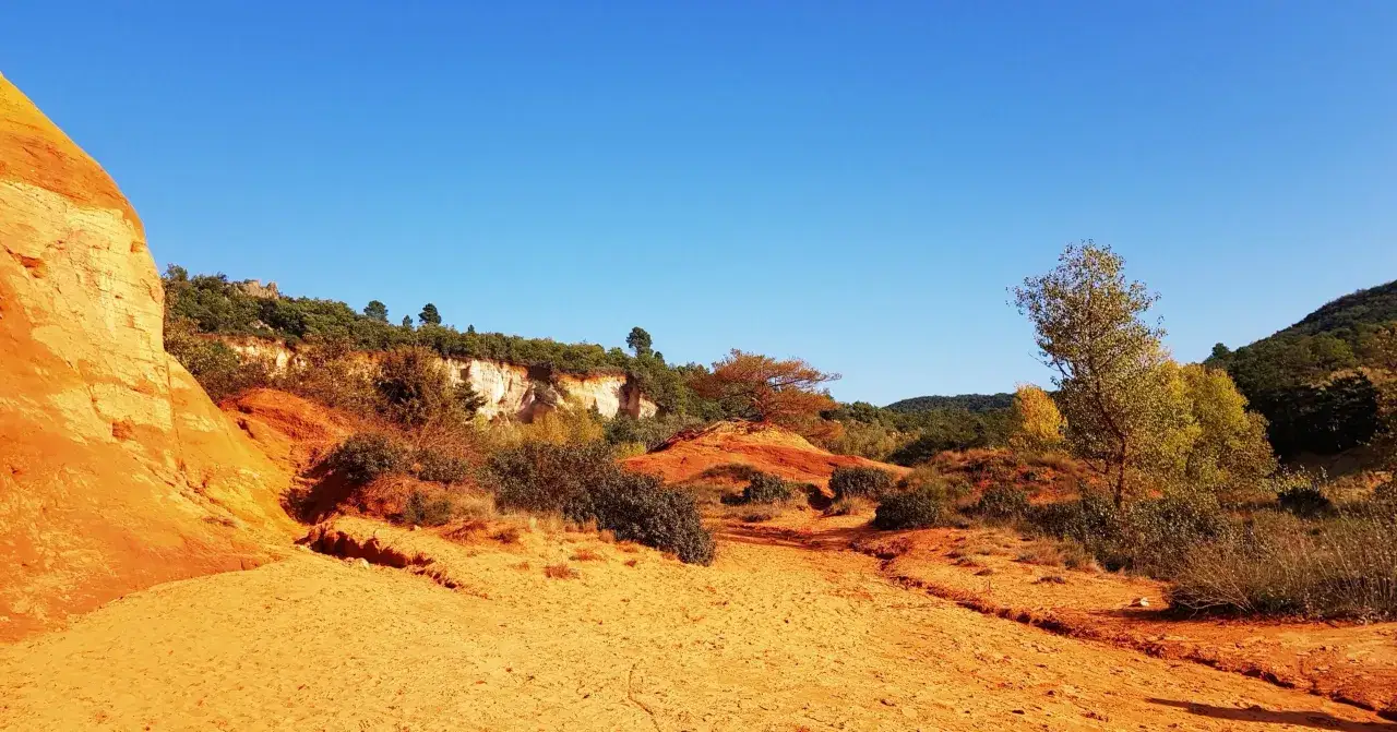 Paysage ocre et rougeoyant du Colorado Proven&ccedil;al, avec des falaises, des arbustes et un ciel bleu intense.