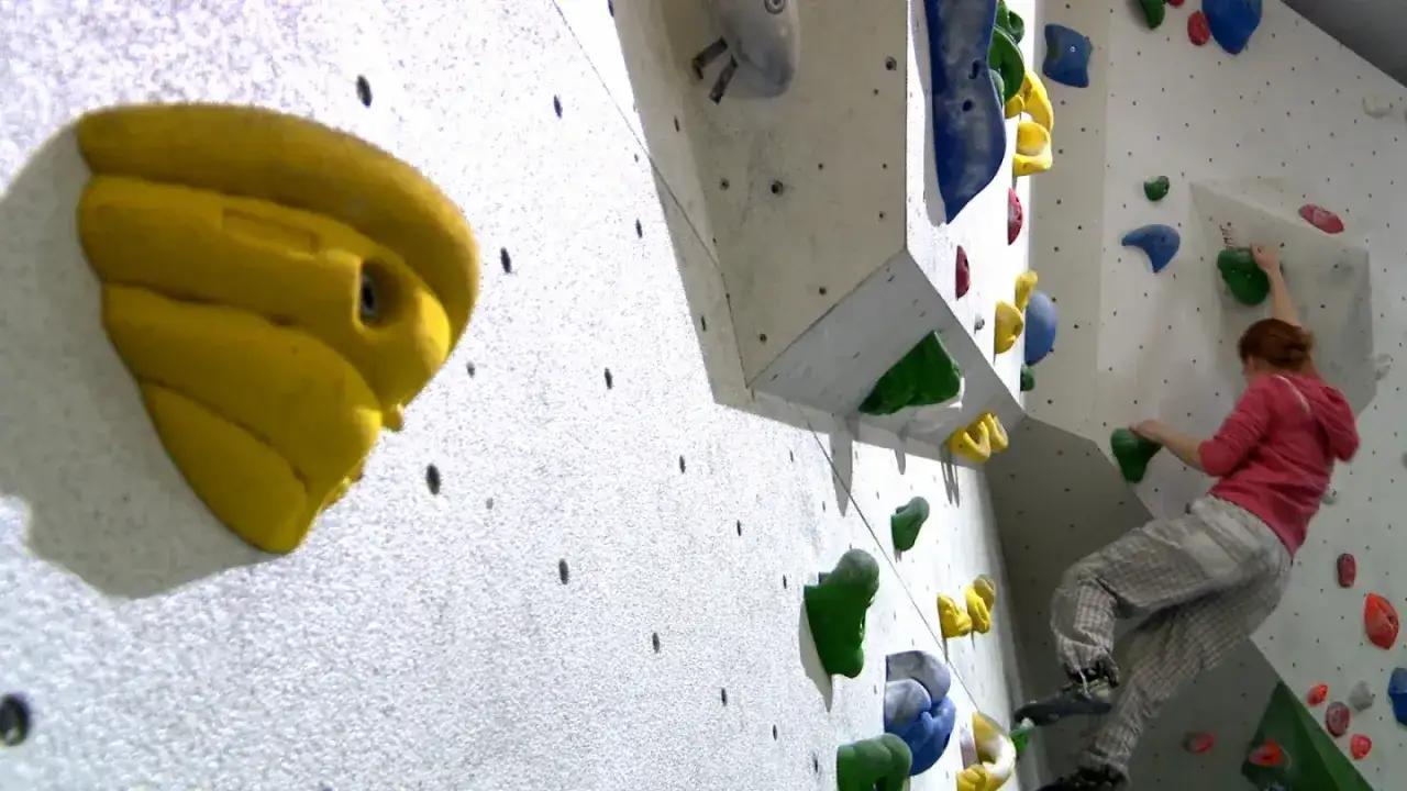 Bouldering co to? Kobieta wspina się po kolorowych chwytach na sztucznej ścianie.
