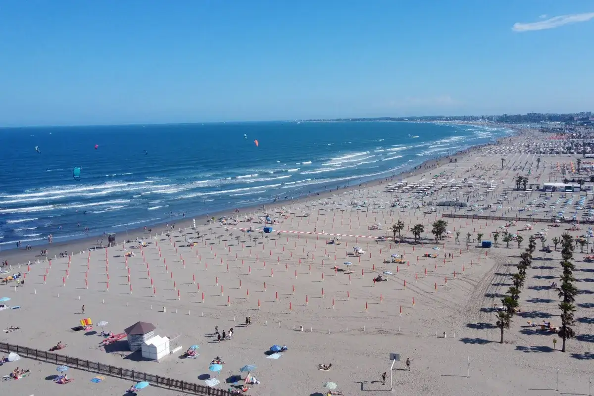 Plage anim&eacute;e &agrave; Chioggia, Italie, avec des parasols, des chaises longues et des kitesurfeurs sur la mer Adriatique.