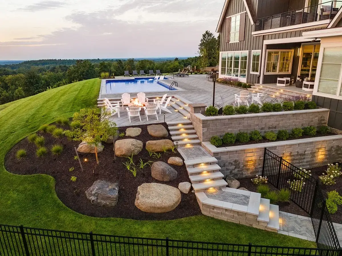 Elegant retaining wall ideas create tiered garden beds and illuminated steps leading to a pool and patio.