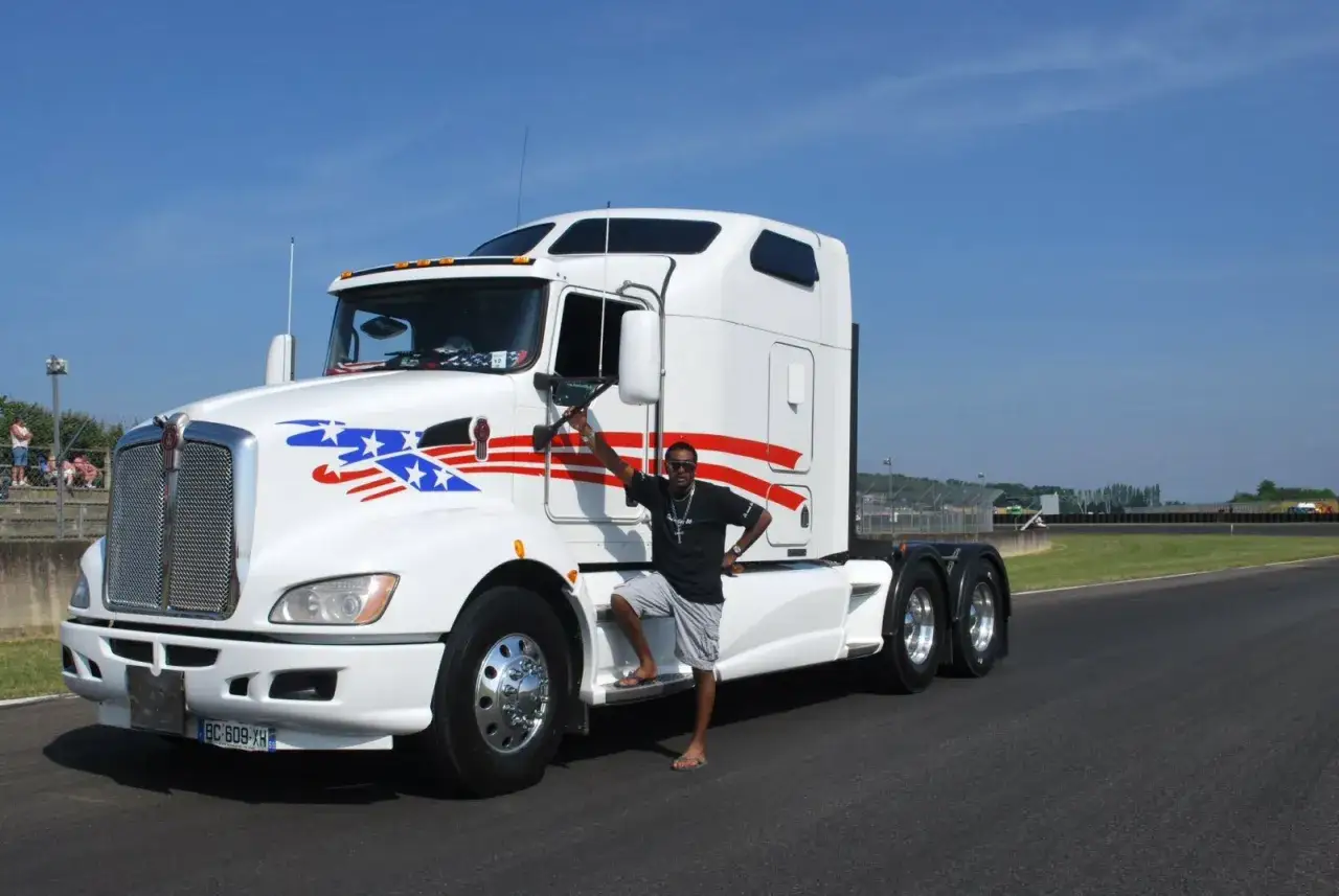 Un homme pose fi&egrave;rement devant un gros camion am&eacute;ricain blanc orn&eacute; d'&eacute;toiles et de rayures.